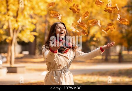 Fröhliche junge Frau im Herbst Outfit fangen gelbe Blätter während Ihr Spaziergang im Park am hellen Herbsttag Stockfoto