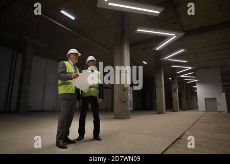 Blick aus der unteren Perspektive auf zwei Geschäftsleute, die auf der Baustelle stehen und Hardhats tragen und Pläne halten, Platz kopieren Stockfoto
