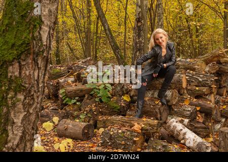 Im Wald steht ein Mädchen in einer Lederjacke und schwarzen Jeans. Schön mit einem freundlichen Blick Stockfoto