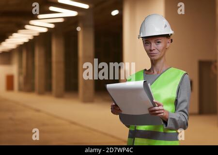 Waist-up-Porträt einer reifen Arbeiterin mit Hardhut und Blick auf die Kamera, während auf der Baustelle im Gebäude stehen, kopieren Raum Stockfoto