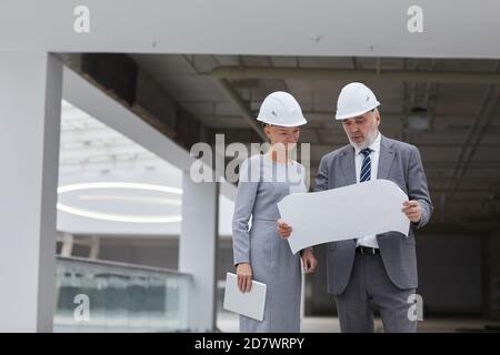 Waist up Porträt der lächelnden Geschäftsfrau Blick auf Pläne auf Baustelle drinnen, kopieren Raum Stockfoto