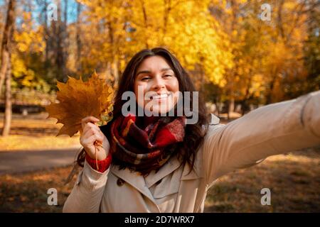 Schöne junge Frau in modischen Herbst Kleidung mit Strauß Herbstlaub und Selfie im Park Stockfoto