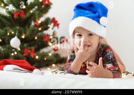 frohe Weihnachten und glückliches neues Jahr, Kindheit, Urlaub Konzept - close-up kleine lustige Mädchen in blau weihnachtsmann Hut auf seinem Bauch spielen und viel Spaß auf dem Bett Stockfoto