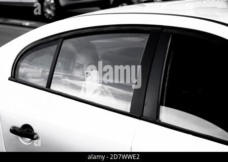 Belgrad, Serbien - 02. Oktober 2020: Hübsche Frau, die auf einem Rücksitz eines weißen Taxiwagens reitet und auf dem Handy schießt, während sie auf eine Kamera schaut Stockfoto