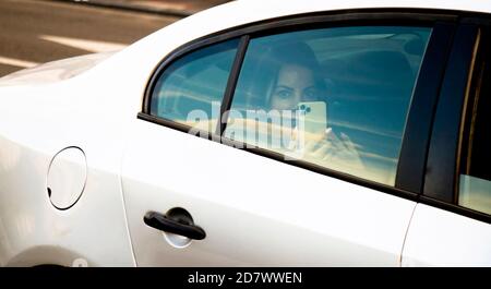 Belgrad, Serbien - 02. Oktober 2020: Hübsche Frau, die auf einem Rücksitz eines weißen Taxiwagens reitet und auf dem Handy schießt, während sie auf eine Kamera schaut Stockfoto