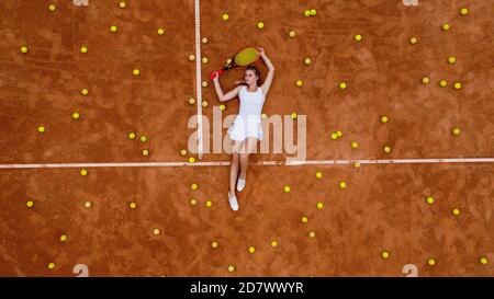 Portrait einer lächelnden Frau, die sich nach hartem Tennistraining im Freien auf dem Tennisplatz mit vielen Bällen und Schlägern entspannt. Dolly-Schuss. Draufsicht Stockfoto