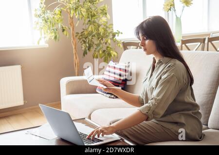 Junge indische Frau hält Rechnung mit Laptop Zahlung Rechnung online zu Hause. Stockfoto