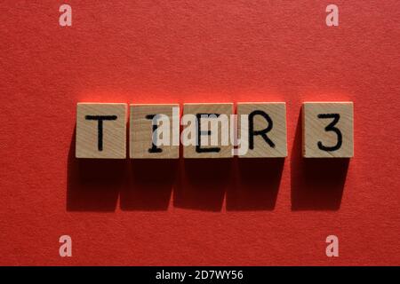 Tier 3, Coronavirus Alarmstufen, Wort in Holzbuchstaben isoliert auf rotem Hintergrund Stockfoto