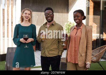 Waist-up-Porträt von zeitgenössischen afroamerikanischen Menschen Blick auf die Kamera Während der Party Wein auf der Außenterrasse genießen Stockfoto