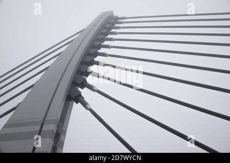 Großer Stahlbogen der Hängebrücke mit Metallseilen schließen Oben im Nebel Stockfoto
