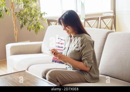 Lächelnde indische Frau, die soziale Medien mit dem Smartphone zu Hause überprüft. Stockfoto