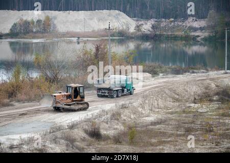 Caterpillar-Lader und Müllkipper arbeiten im Tagebau. Schwere Maschinen im Tagebau am Fluss. Planierraupe und LKW beim Graben und Bagger Stockfoto