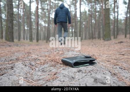 Der junge Junge verliert seine Geldbörse mit Euro-Geldscheinen auf dem russischen Herbst-Tannenholz-Weg. Unachtsamkeit und Verlust des Portemonnaie Konzepts Stockfoto