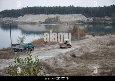 Caterpillar-Lader und Müllkipper arbeiten im Tagebau. Schwere Maschinen im Tagebau am Fluss. Planierraupe und LKW beim Graben und Bagger Stockfoto