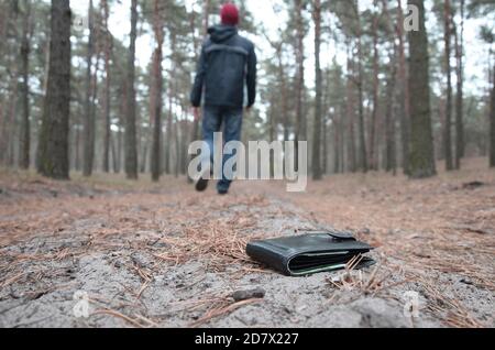 Der junge Junge verliert seine Geldbörse mit Euro-Geldscheinen auf dem russischen Herbst-Tannenholz-Weg. Unachtsamkeit und Verlust des Portemonnaie Konzepts Stockfoto