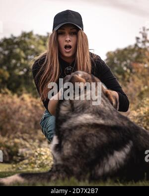 Vertikale Aufnahme einer Frau, die einen schockierten Ausdruck macht, als sie versucht, den Stock aus dem Mund des Hundes zu ziehen. Spielen Sie ein Spiel von fetch und der Hund gewann Stockfoto