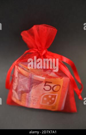 Eine hübsche kleine rote Geschenktasche isoliert mit Seidenbändern mit Bargeld gefüllt. 50-Dollar-Note sichtbar und Wads von anderen farbigen Noten. Stockfoto