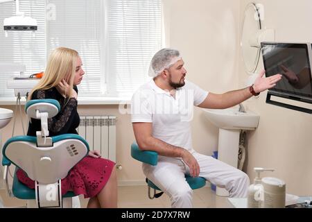 Zahnarzt, der mit dem Patienten spricht und auf einen leeren Monitor zeigt Stockfoto