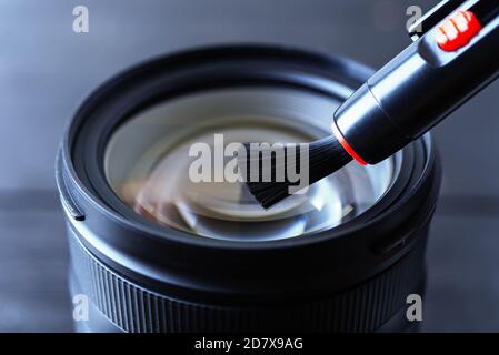 Entfernen von Staub von der Frontlinse mit der Linsenstiftbürste. Routinemäßige Entfernung von Staub und Flecken von fotografischen Geräten. Nahaufnahme der Wartung. Draufsicht. Stockfoto