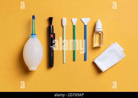 Luftgebläse, Linsenstift, drei verschiedene Tupfer, Flüssigkeitssensor-Reiniger und Mikrofaser auf gelbem Hintergrund. Reinigungsset für Fotoausrüstung. Stockfoto