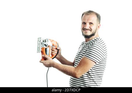 Ein lächelnder Mann in einem gestreiften T-Shirt hält eine elektrische Stichsäge in den Händen. Isoliert auf weißem Hintergrund Stockfoto