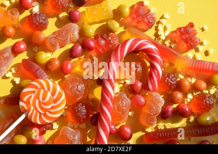 Bonbons mit Gelee und Zucker. Bunte Palette von verschiedenen Kindern Süßigkeiten und Leckereien auf gelbem Hintergrund. Rote Marmelade in Form eines Herzens mit einem Stockfoto