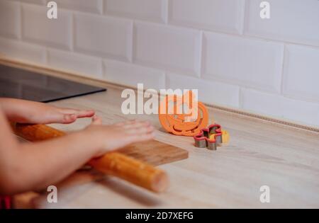 Kleine Kinderhände machen traditionelle Halloween-Kekse. Roher Teig und Ausstecher für die Ferienkekse auf Holztischuntergrund. Cookies werden vorbereitet Stockfoto