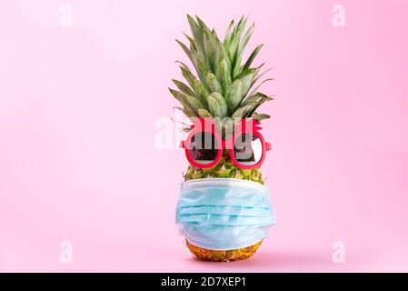 COVID Travel Konzept. Ananas in Sonnenbrille und medizinische Maske auf rosa Hintergrund. Ananas in rosa Sonnenbrille und Gesichtsmaske - Neue normale Reise Stockfoto