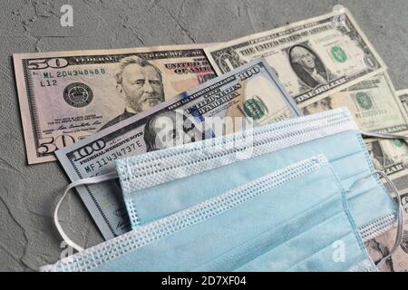 Amerikanische Dollar und schützende medizinische Masken sind auf einem grauen Betonhintergrund. Geld ist in der modernen Welt während der Zeit der Quarantäne und der Stockfoto