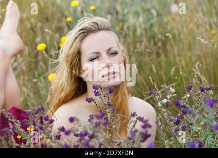 Künstlerische Porträt der Sommersprossen Frau auf natürlichen Hintergrund. Junge Frau genießt die Natur zwischen den Blumen und Gras. Nahaufnahme Sommerportrait Stockfoto