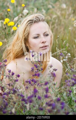 Künstlerische Porträt der Sommersprossen Frau auf natürlichen Hintergrund. Junge Frau genießt die Natur zwischen den Blumen und Gras. Nahaufnahme Sommerportrait Stockfoto