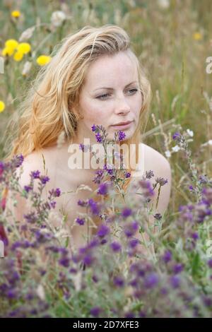 Künstlerische Porträt der Sommersprossen Frau auf natürlichen Hintergrund. Junge Frau genießt die Natur zwischen den Blumen und Gras. Nahaufnahme Sommerportrait Stockfoto