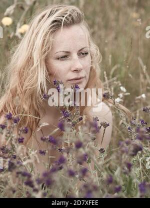 Künstlerische Porträt der Sommersprossen Frau auf natürlichen Hintergrund. Junge Frau genießt die Natur zwischen den Blumen und Gras. Nahaufnahme Sommerportrait Stockfoto