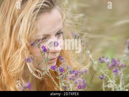 Künstlerische Porträt der Sommersprossen Frau auf natürlichen Hintergrund. Junge Frau genießt die Natur zwischen den Blumen und Gras. Nahaufnahme Sommerportrait Stockfoto