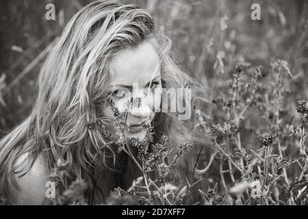 Künstlerische Porträt der Sommersprossen Frau auf natürlichen Hintergrund. Junge Frau genießt die Natur zwischen den Blumen und Gras. Nahaufnahme Sommerportrait Stockfoto