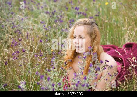 Künstlerische Porträt der Sommersprossen Frau auf natürlichen Hintergrund. Junge Frau genießt die Natur zwischen den Blumen und Gras. Nahaufnahme Sommerportrait Stockfoto