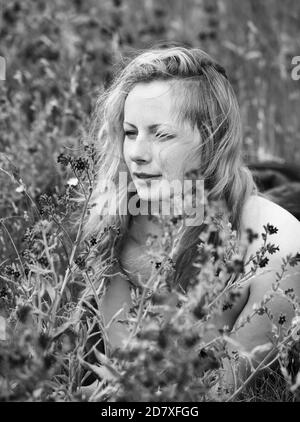 Schwarz-Weiß-Porträt von Sommersprossen Frau auf natürlichem Hintergrund. Junge Frau genießt die Natur zwischen den Blumen und Gras. Nahaufnahme Sommerportrait Stockfoto