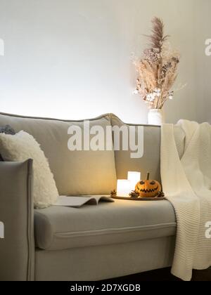 Gemütliche skandinavische Stil halloween-Interieur. Leuchtender orangefarbener Kürbis mit Jack-o-Laterne lachendem Gesicht, Kerzen auf dem Sofa. Vertikal. Speicherplatz kopieren. Stockfoto