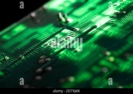 Detail einer beleuchteten grünen Elektronikplatine mit vielen elektrischen Komponenten, isoliert auf schwarzem Hintergrund Stockfoto