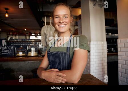 Fröhliche junge Kellnerin mit Schürze auf dem Tisch stehend Im Café Stockfoto