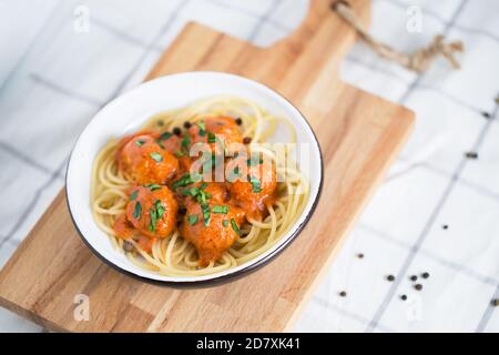 Fleischbällchen in Tomatensauce mit Pasta auf dem weißen Teller Auf dem Kochbrett mit Zwiebelauflage und Pfeffer Stockfoto