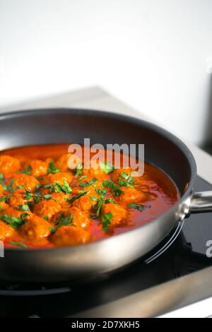 Fleischbällchen in Tomatensauce mit grüner Zwiebelauflage und Petersilie In der schwarzen Pfanne Stockfoto