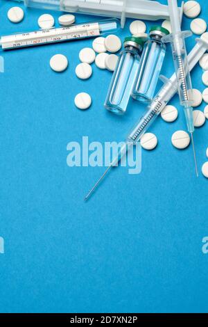 Draufsicht auf Pillen, Spritze, Thermometer und Ampulle mit Impfung auf blauem Hintergrund mit Kopierraum Stockfoto