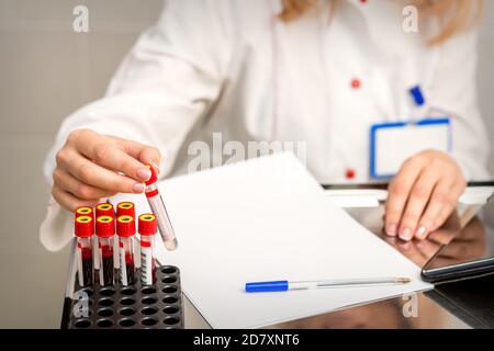 Die Hand eines Laboranten oder Pflegepersonals nimmt einen leeren Bluttest ab Röhre aus dem Rack im Forschungslabor Stockfoto