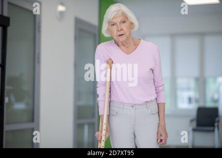 Grauhaarige Frau in rosa Hemd zu Fuß mit einer Krücke Stockfoto
