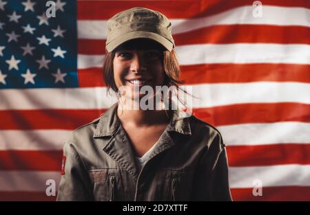 Feier in den USA. Porträt einer lächelnden Soldatinnen, die vor dem Hintergrund der amerikanischen Flagge posiert. Stockfoto