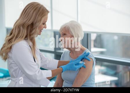 Langhaarige lächelnde Krankenschwester, die eine ältere Frau impfen lässt Stockfoto