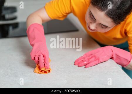 Eine junge Frau in Gummihandschuhen wischt den Tisch mit einem Lappen eifrig ab. Nahaufnahme im Hochformat von oben. Hausarbeit. Stockfoto