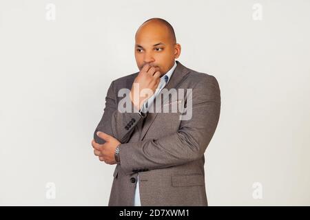 Porträt eines unglücklichen jungen afroamerikanischen Geschäftsmann, sieht angespannt und nervös mit seinen Händen auf dem Mund beißen seine Nägel. Angstproblem. Stehen auf einem grauen Hintergrund Stockfoto