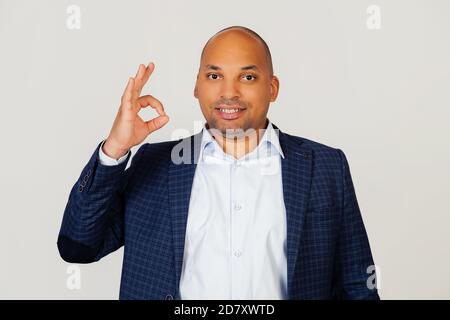 Porträt eines jungen afroamerikanischen Kerl Geschäftsmann, lächelnd positiv, so dass okay Zeichen mit Hand und Fingern. Glücklicher Ausdruck. Stehen auf einem grauen Hintergrund Stockfoto